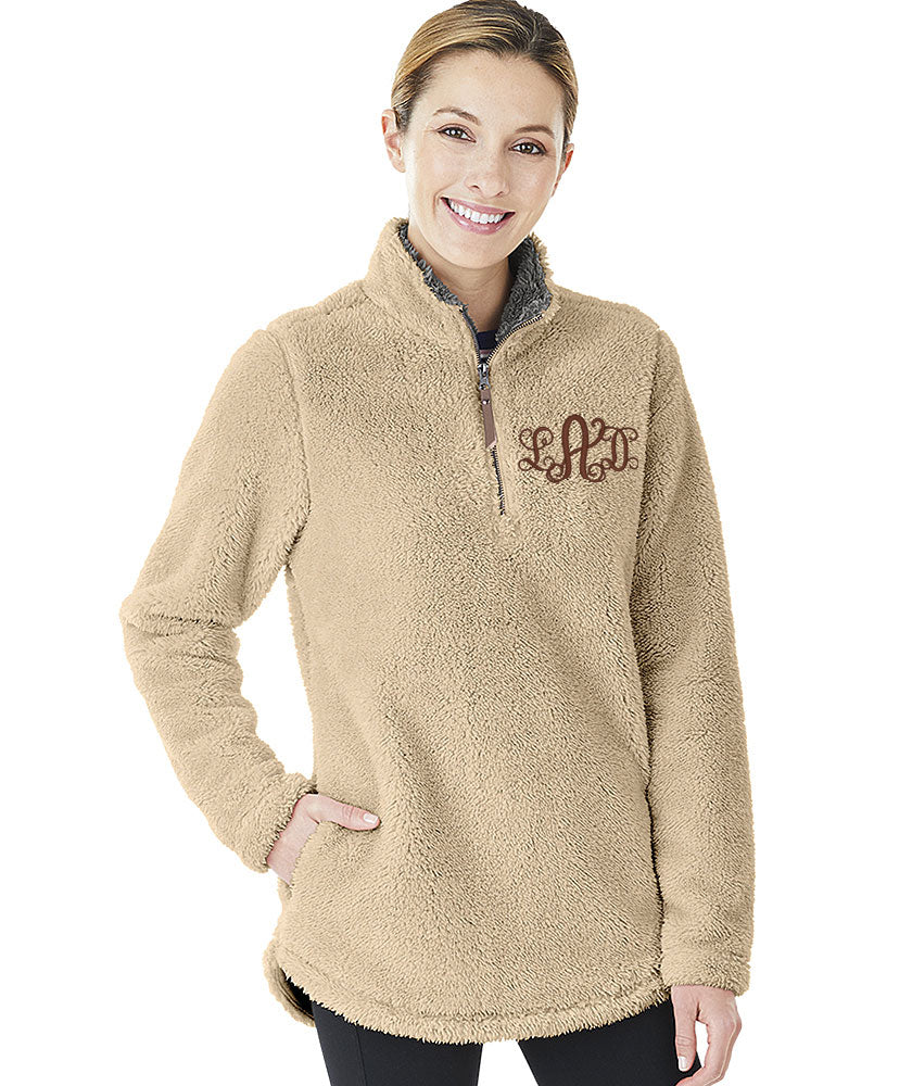 A woman wearing a tan, fuzzy quarter-zip pullover with a brown embroidered monogram on the chest.