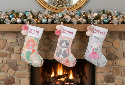 Three personalized stockings with mermaid, cat, and mouse designs, embroidered names Ellie, Emma, Harper, and pink pom-poms.