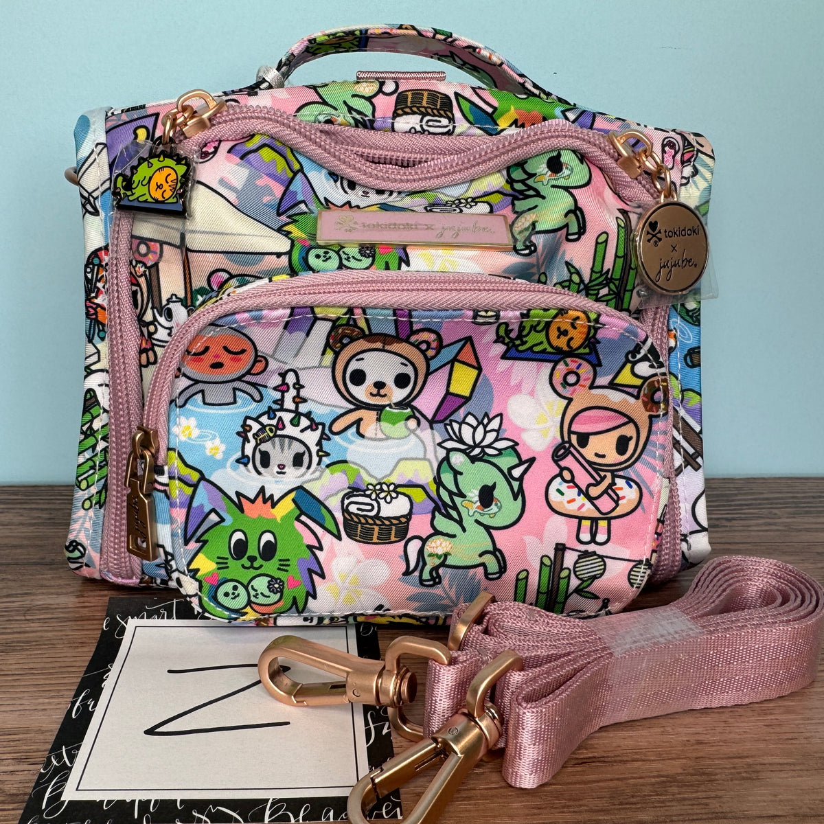 Colorful Tokidoki x Ju-Ju-Be Mini BFF bag featuring cartoon character print in pink, purple, and green with detachable pink shoulder strap