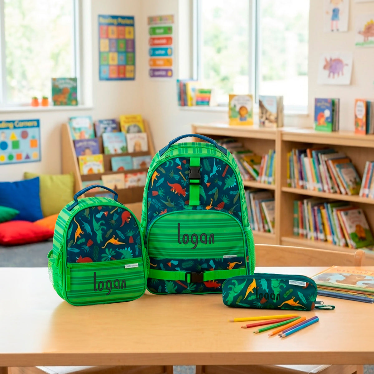 Green Stephen Joseph dinosaur-print backpack, lunchbox, and pencil pouch set, each personalized with embroidered name "logan" in dark green script