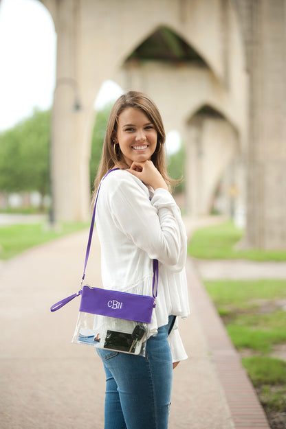 Woman wearing a purple and clear crossbody purse with the monogram 'CBN' embroidered on the front.