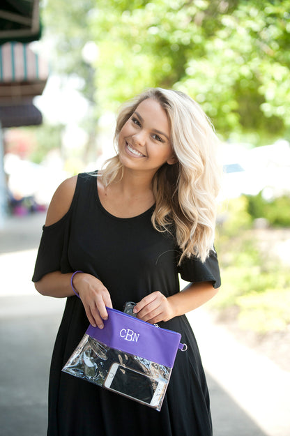 Woman holding a clear crossbody purse with a purple top and white monogram 'CBN'.