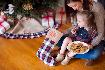 Burlap Christmas tree skirt with plaid ruffle beneath a tree beside a child holding a matching stocking