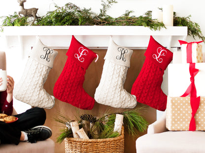 Two cream and two red monogrammed cable knit stockings hanging beneath a holiday garland