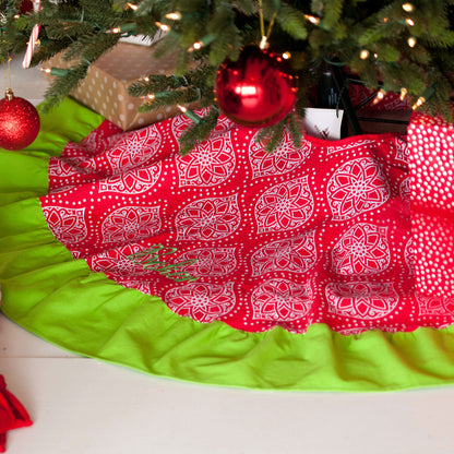 Red and white Noel patterned Christmas tree skirt with green ruffle beneath a decorated tree