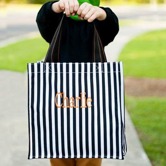 Child holding a black and white vertical striped tote with the name Charlie embroidered in orange