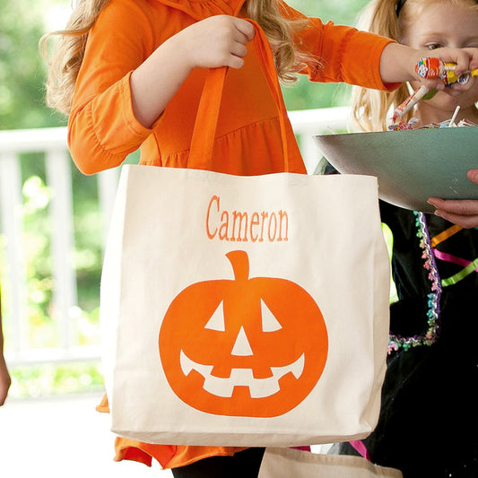 Child in an orange dress holding the pumpkin tote with the name Cameron while reaching for candy on a porch
