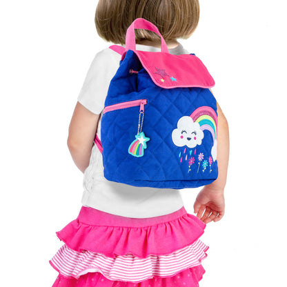 Toddler wears quilted blue backpack with pink flap, embroidered smiling cloud, rainbow, flowers, and dangling unicorn charm; white shirt and pink ruffled skirt