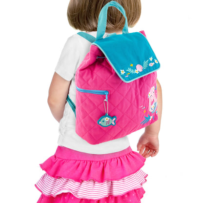 Toddler wearing pink quilted backpack with teal flap, embroidered mermaid and flowers, fish zipper pull, worn over white shirt and pink ruffled skirt