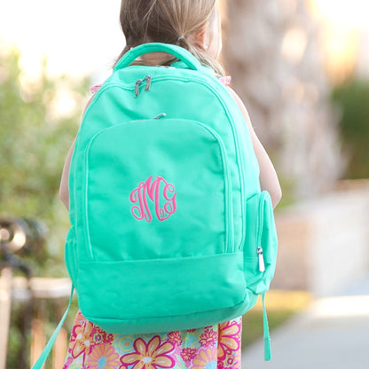 Child wearing a mint backpack with a pink monogram