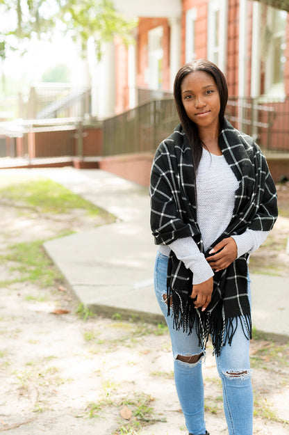 Woman wearing a black and white plaid scarf with fringe over a white sweater and jeans.