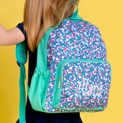 Back view of a child wearing a blue confetti-print preschool backpack with mint trim