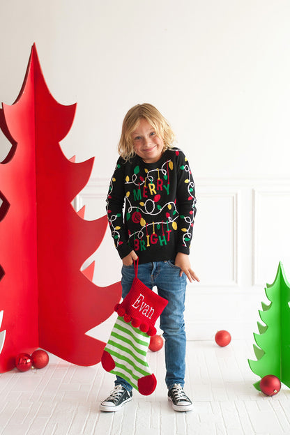 Child holding a green and white striped knit stocking with red cuff and pom-poms