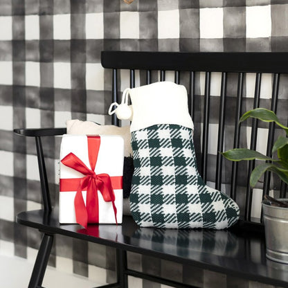 Green and cream check knit stocking with cream cuff on a black bench beside a wrapped gift