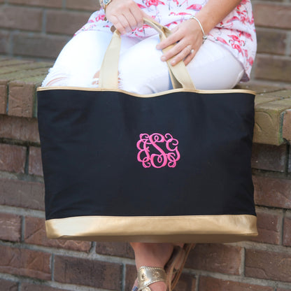 Black tote with gold-colored trim and a pink monogram held while seated