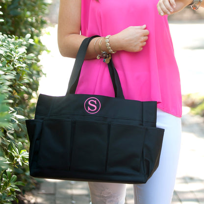 Woman holding a black carryall tote with a pink initial