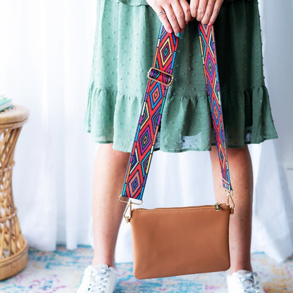 Tan leather wristlet with a colorful geometric patterned strap held by a person in a green dress.