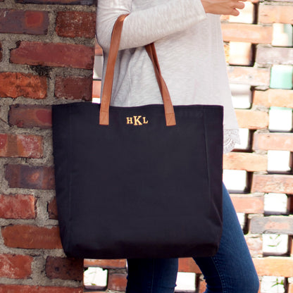 Black tote with tan handles and gold-colored initials held by a woman