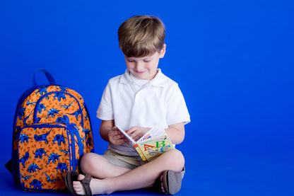 Orange dinosaur-print backpack beside a child reading a book
