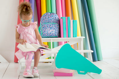 Confetti-print preschool backpack beside a child and colorful classroom props