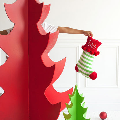 Green striped knit stocking with red embroidered cuff held beside red and green tree decorations