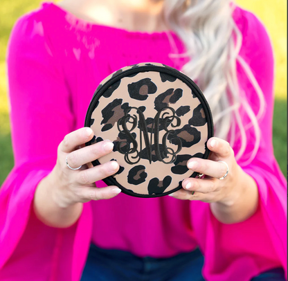Woman holding a tan leopard-print jewelry case with a black monogram