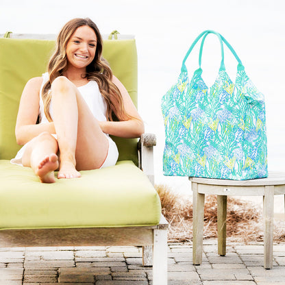 Mint coral-print beach bag beside a woman on a lounge chair
