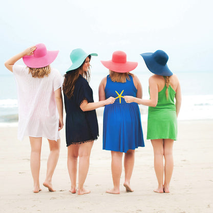 Four women wearing colorful wide-brim hats at the beach