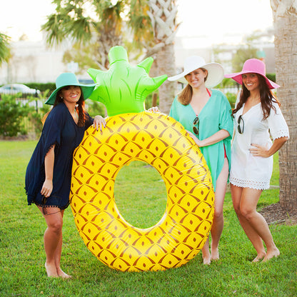 Women wearing floppy hats beside a pineapple-shaped pool float