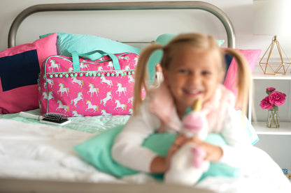 Pink unicorn travel bag on a bed behind a child