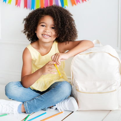Child seated beside a cream Charlie backpack