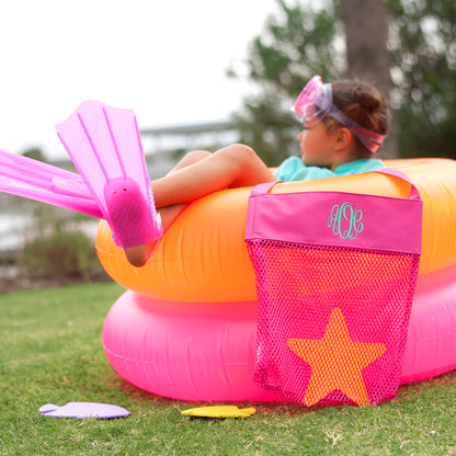 Hot pink mesh tote with a monogram beside colorful pool floats