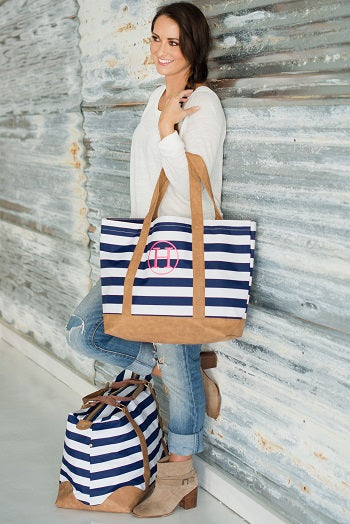 Woman carrying a navy striped tote with tan trim beside a matching travel bag