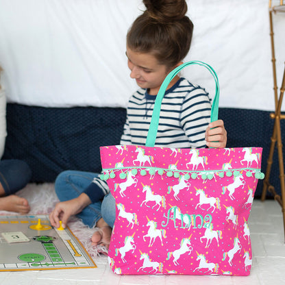 Child holding a pink unicorn tote with mint handles beside a book