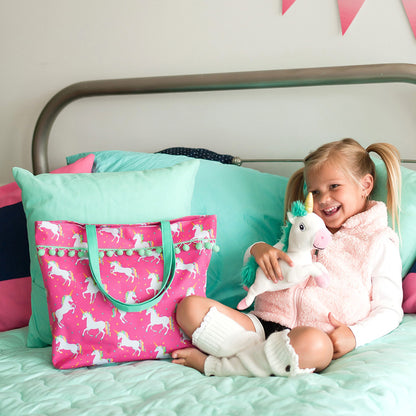Pink unicorn tote with a personalized name beside a child on a bed