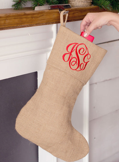 Natural burlap Christmas stocking with a red embroidered monogram hanging from a mantel