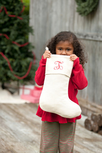 Child holding a cream Christmas stocking with embroidered monogram