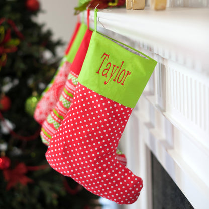 Red Christmas stocking with white dots and green embroidered cuff hanging from a mantel