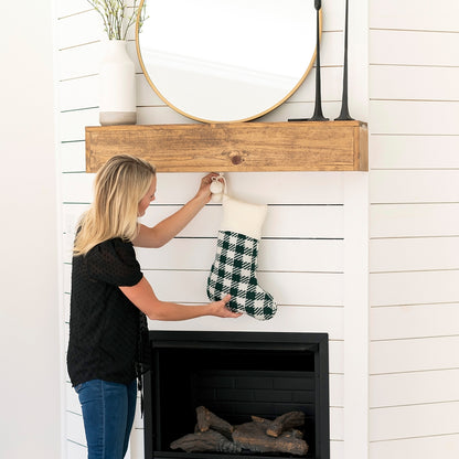 Woman hanging a green check knit stocking with cream cuff from a mantel