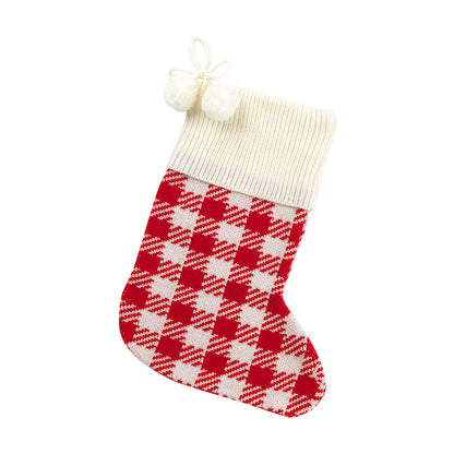 Red and cream houndstooth knit Christmas stocking with cream cuff and pom-poms on white