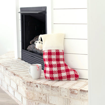 Red and cream check knit stocking with cream cuff displayed on a brick hearth
