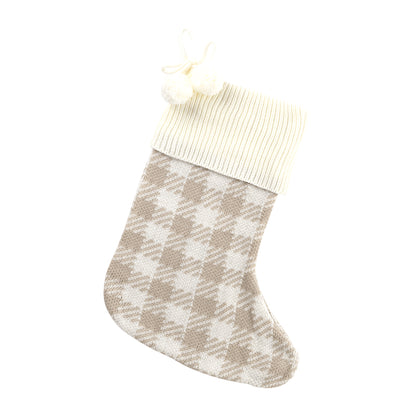 Tan and cream houndstooth knit Christmas stocking with cream cuff and pom-poms on white