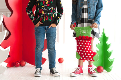 Child holding a red dotted knit stocking with green cuff and red pom-poms