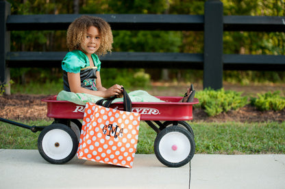 Orange tote bag with large white polka dots, black handles with orange stitching, three quarter view on white
