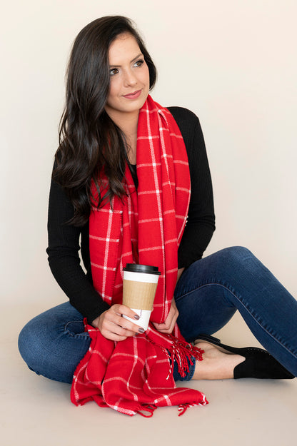 Woman wearing a red and white plaid scarf with fringe, holding a coffee cup.