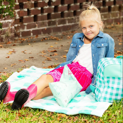 Mint checked travel bag beside a child resting on a blanket outdoors