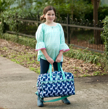 Child holding a navy llama-print travel bag outdoors