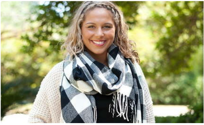 Woman wearing a black, white, and gray buffalo check scarf with fringe.