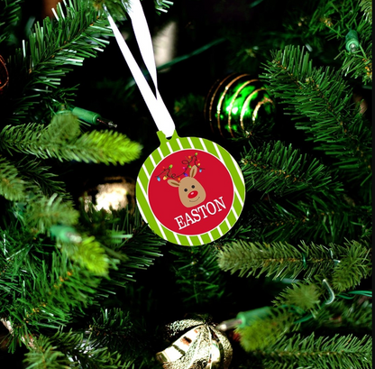 Reindeer Christmas ornament with green and white striped border, red center and personalized name hanging from a white ribbon on a tree