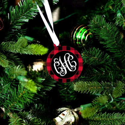 Red and black buffalo check ornament with white monogram hanging from a white ribbon on a Christmas tree